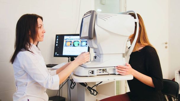 Modern ophthalmologist examining attractive womans eyes with modern hi-tech equipment - Foto, afbeelding