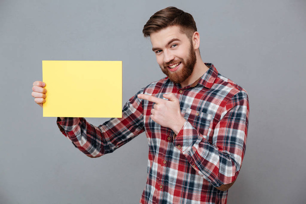 Smiling young bearded man holding copyspace blank - Zdjęcie, obraz