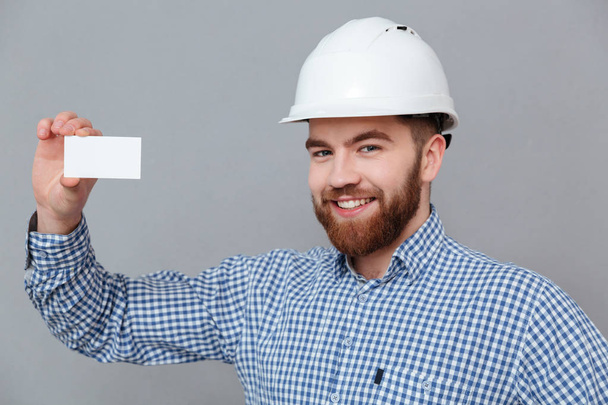 Happy bearded builder holding copyspace business card - Photo, image