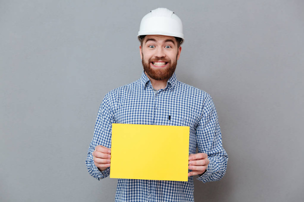 Cheerful bearded man builder holding copyspace blank - Zdjęcie, obraz