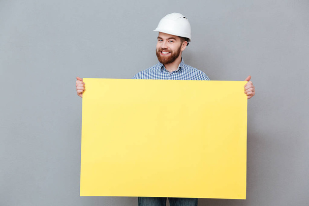Happy young bearded builder holding copyspace board - Zdjęcie, obraz