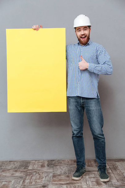 Happy young bearded builder holding copyspace board - Valokuva, kuva