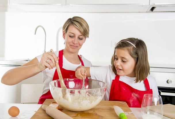 νεαρή μητέρα και κορούλα γλυκό σε μάγειρας ποδιά μαγειρικής μαζί ψήσιμο σε μοντέρνα κουζίνα στο σπίτι - Φωτογραφία, εικόνα