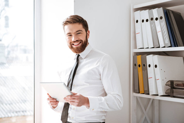 Happy young businessman holding tablet and look at camera. - Photo, Image