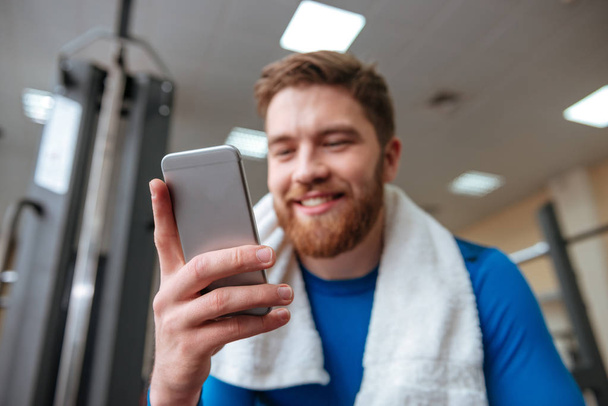 Happy young sportsman in gym looking at phone. - Φωτογραφία, εικόνα