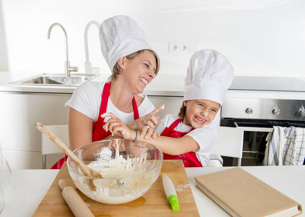 jovem mãe e pequena filha doce no chapéu de cozinheiro e avental cozinhar juntos assar em casa cozinha
 - Foto, Imagem