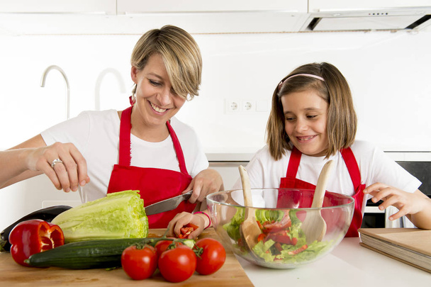 Mutter und kleine Tochter kochen gemeinsam mit Kochschürze Salat in der heimischen Küche - Foto, Bild