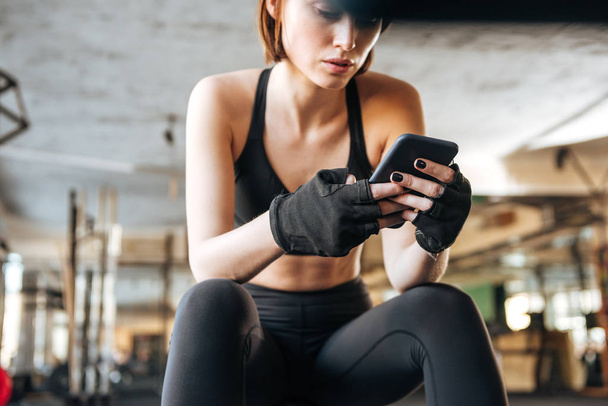 Woman athlete sitting and using smartphone in gym - Valokuva, kuva