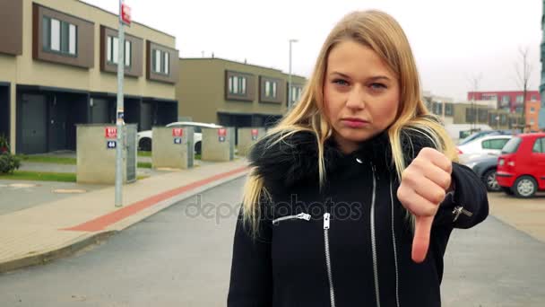 Een mooie, jonge vrouw staat op de straat in een voorstedelijk gebied, toont een duim naar de camera en schudt haar hoofd - Video