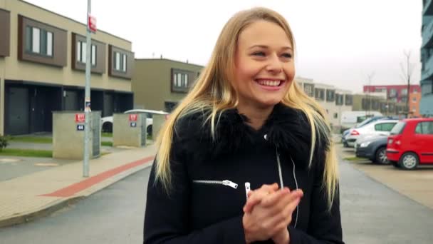 Μια νεαρή, όμορφη γυναίκα στέκεται στον δρόμο σε μια προαστιακή περιοχή και γιορτάζει, κτίρια στο παρασκήνιο - Πλάνα, βίντεο