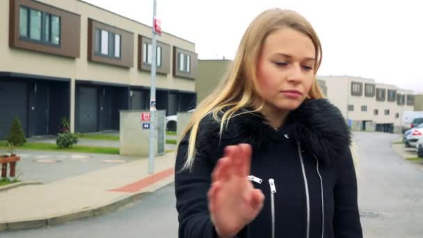 Een mooie, jonge vrouw staat op de straat in een voorstedelijk gebied, schudt haar hoofd en toont een gebaar van weigering - Video