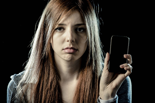 worried teenager holding mobile phone as internet addict and victim of cyber bullying - Photo, Image