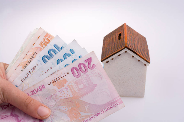 Hand holding Turkish Lira banknotes by the side of a model house on white background - Photo, Image