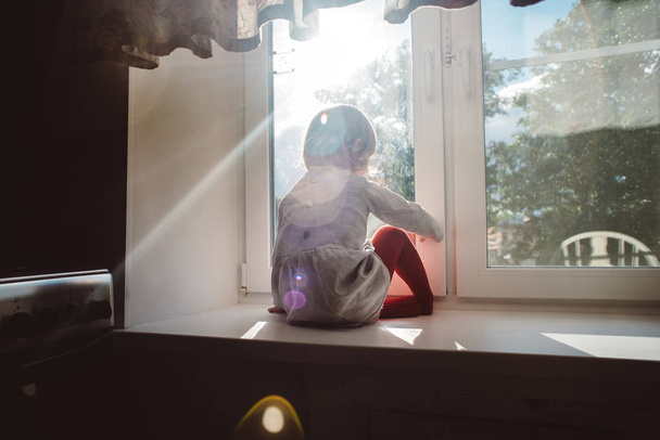Little girl sits on a windowsill - Фото, изображение