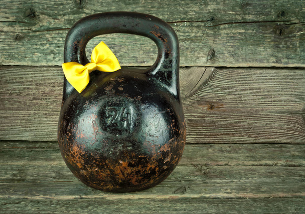 Vintage old kettlebell with a yellow tied bow on a wooden background. - Photo, Image