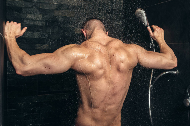 Muscular fitness bodybuilder taking a shower after training. Close up details of back muscles in shower - Foto, imagen