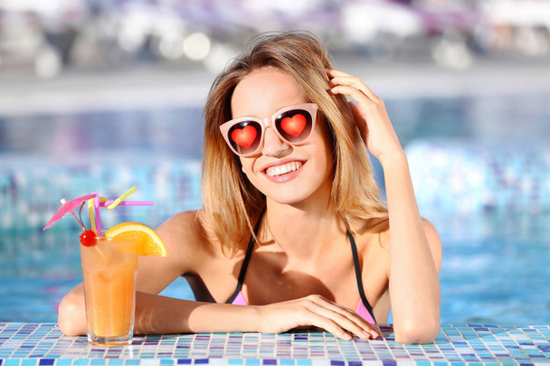 Young beautiful woman wearing sunglasses with hearts in swimming pool - Foto, afbeelding