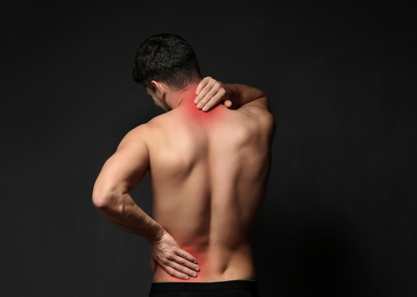 Young man suffering from back pain on black background. Health care concept - Фото, зображення