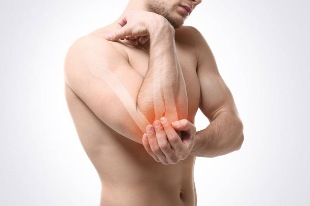Young man suffering from elbow pain on light background. Health care concept - Valokuva, kuva