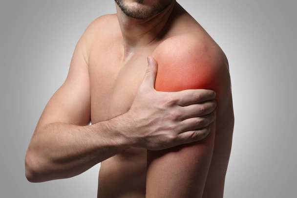 Young man suffering from shoulder pain on gray background. Health care concept - Valokuva, kuva