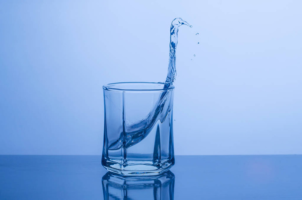Splash in a glass of water on a blue background - Foto, Imagem