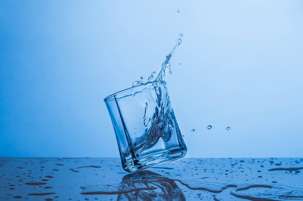 Splash in a glass of water on a blue background - Foto, afbeelding