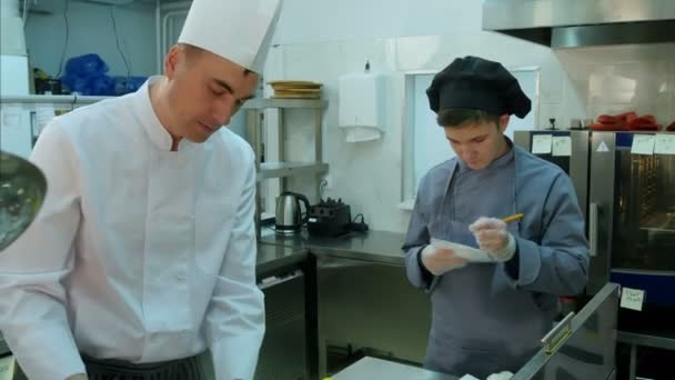 Junge Auszubildende beobachten, wie Koch kocht und Notizen macht - Filmmaterial, Video
