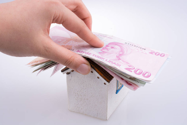 Hand hält türkische Lira-Banknoten auf dem Dach eines Musterhauses auf weißem Hintergrund - Foto, Bild