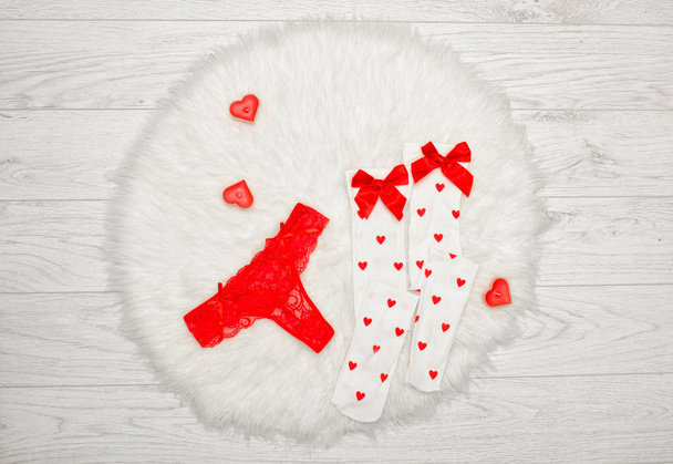 Fashion concept. Red thong panties and white stockings with bows, candles in the shape of a heart on a white fur. View from above - Foto, immagini