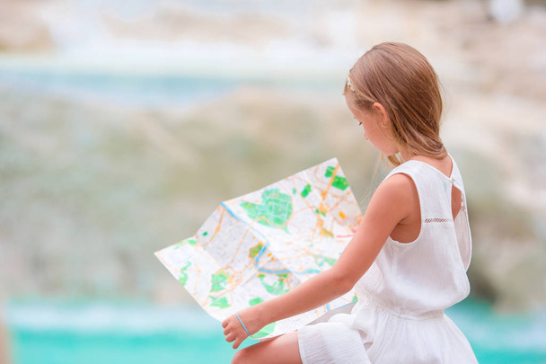 Adorable girl looking at touristic map near Trevi Fountain, Rome. Happy toodler kid enjoy italian vacation in Europe. - Photo, Image