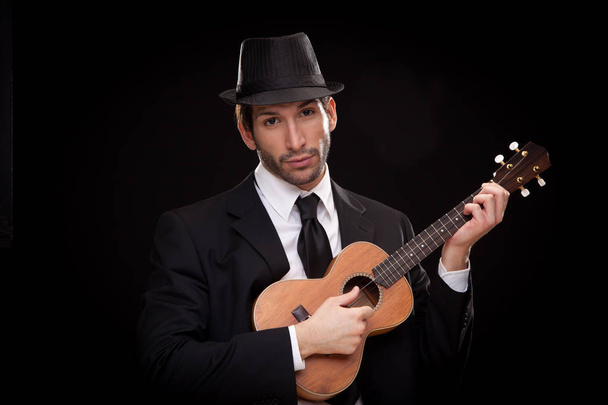 elegant happy man singer musician playing ukulele guitar isolated on black - Fotografie, Obrázek