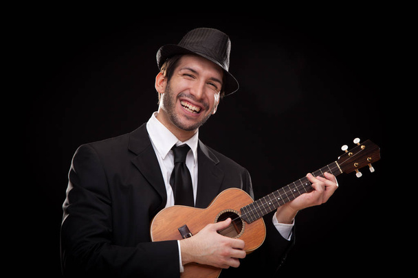 elegant happy man singer musician playing ukulele guitar isolated on black - Foto, Bild
