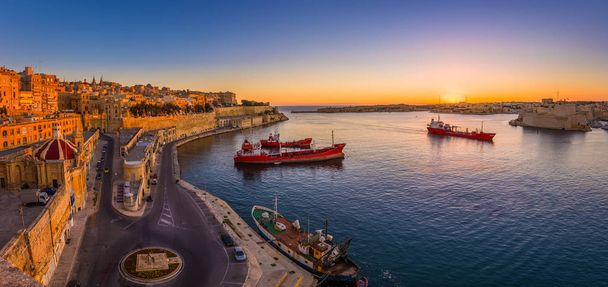 Valletta, Malta - Fotografia panorâmica de um incrível nascer do sol de verão no Grande Porto de Valletta com navios e as antigas casas e paredes da capital maltesa
. - Foto, Imagem