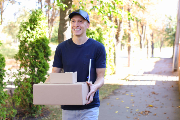 Postbote trägt Päckchen in Händen und lächelt in Kamera - Foto, Bild