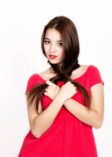 beautiful young woman dressed in a red dress, holds pigtails. studio shot - Φωτογραφία, εικόνα