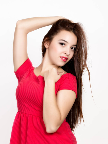 beautiful young woman dressed in a red dress, holds pigtails. studio shot - Фото, зображення