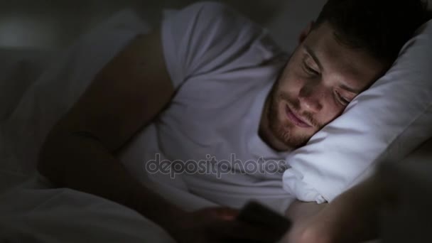 young man with smartphone in bed at night - 映像、動画