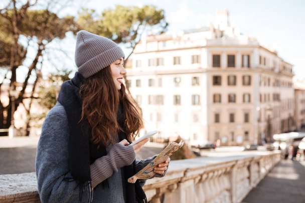 Smiling woman with map and mobile phone standing in city - Photo, Image