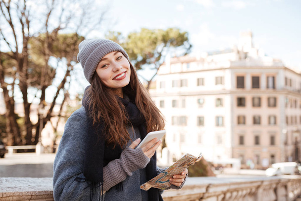Cheerful woman using cell phone and map in the city - Foto, immagini