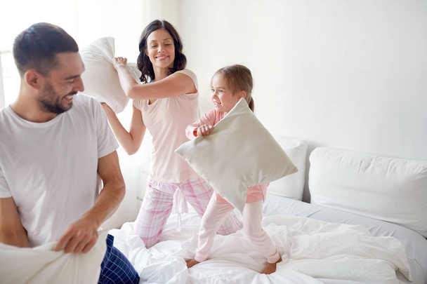 happy family having pillow fight in bed at home - 写真・画像