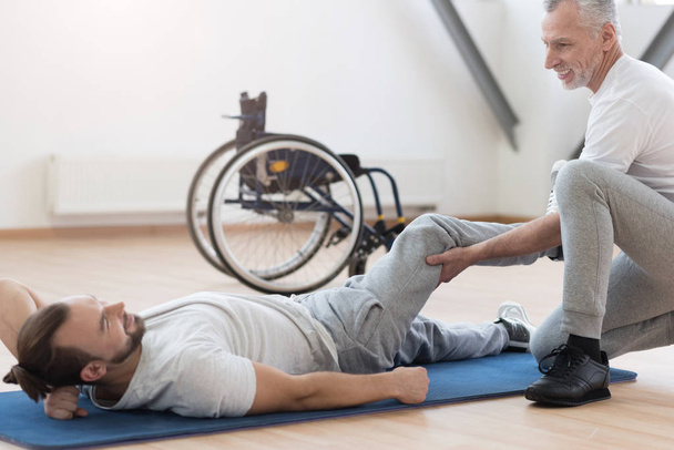 Friendly orthopedist stretching the disabled individual in the gym - Fotó, kép