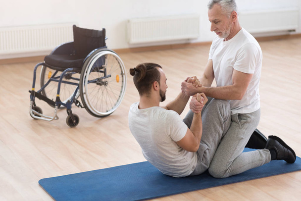Skilled orthopedist assisting the disabled in the gym - Fotó, kép