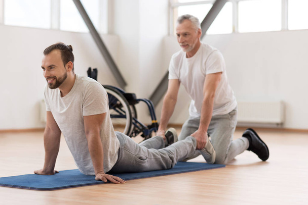 Cheerful physical therapist stretching the handicapped in the gym - Foto, imagen