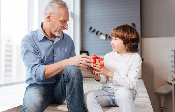 Cheerful elderly man giving a present to his grandson - Foto, afbeelding