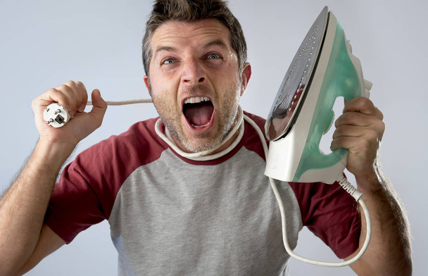 young crazy desperate and frustrated man doing housework holding iron - Photo, Image
