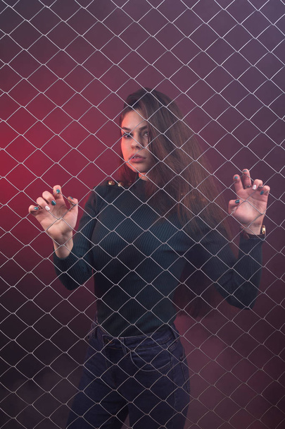 Girl standing behind the mesh fence - Zdjęcie, obraz
