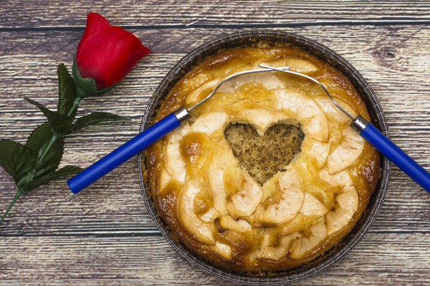 Apfelkuchen mit einer Mulde in der Form eines Herzens und zwei Gabeln in - Foto, Bild