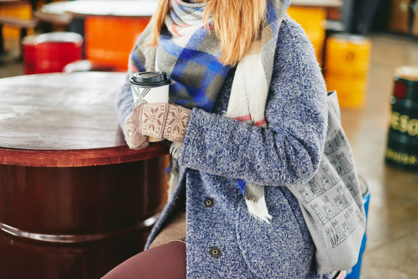 Girl in grey coat, hat and blanket scarf with cup of coffee in cafe - Photo, Image