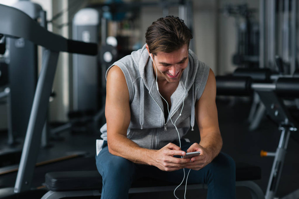 Healthy fitness man using smartphone in the gym, texting message - Zdjęcie, obraz