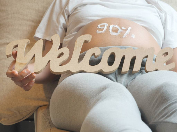 Pregnancy health concept nearly to delivery. Belly of a pregnant woman with cream and welcome message. - Photo, Image